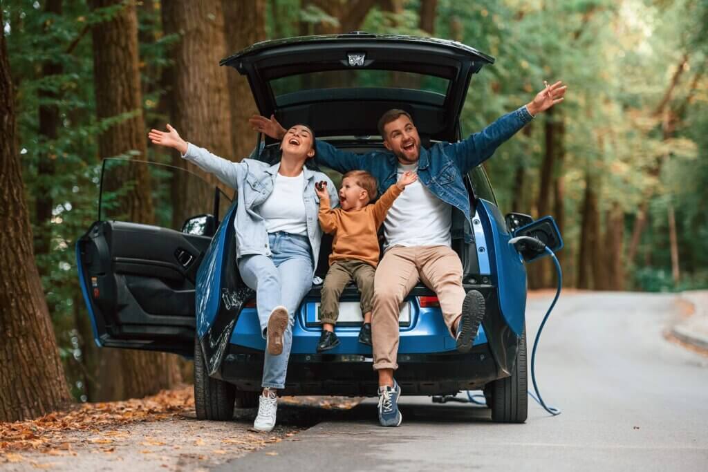 Familie fericită în natură, lângă mașină electrică.